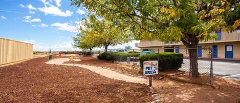 A motel with a pet area sign, a fenced parking lot, and a building with a blue awning.