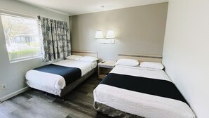 A hotel room with two beds, a window with patterned curtains, a nightstand with a lamp, and a view of the outside. - Motel 6 Holbrook, AZ (Holbrook)