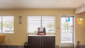 A coffee station with a coffee machine and cups, a trash bin, and a door leading outside. - Motel 6 Holbrook, AZ (Holbrook)