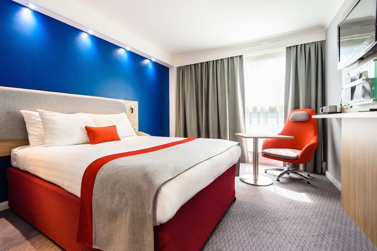 Ein Hotelzimmer mit Bett, Schreibtisch, Stuhl und Fernseher.