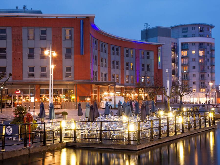 A waterfront restaurant with outdoor seating, a canal, and modern buildings in the background.