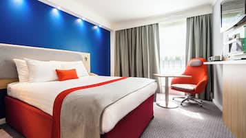 Una camera d'albergo con un letto, una scrivania, una sedia e una finestra con tende.