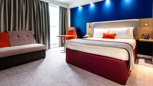 Una habitación de hotel moderna con una cama grande, un sofá y una mesita.