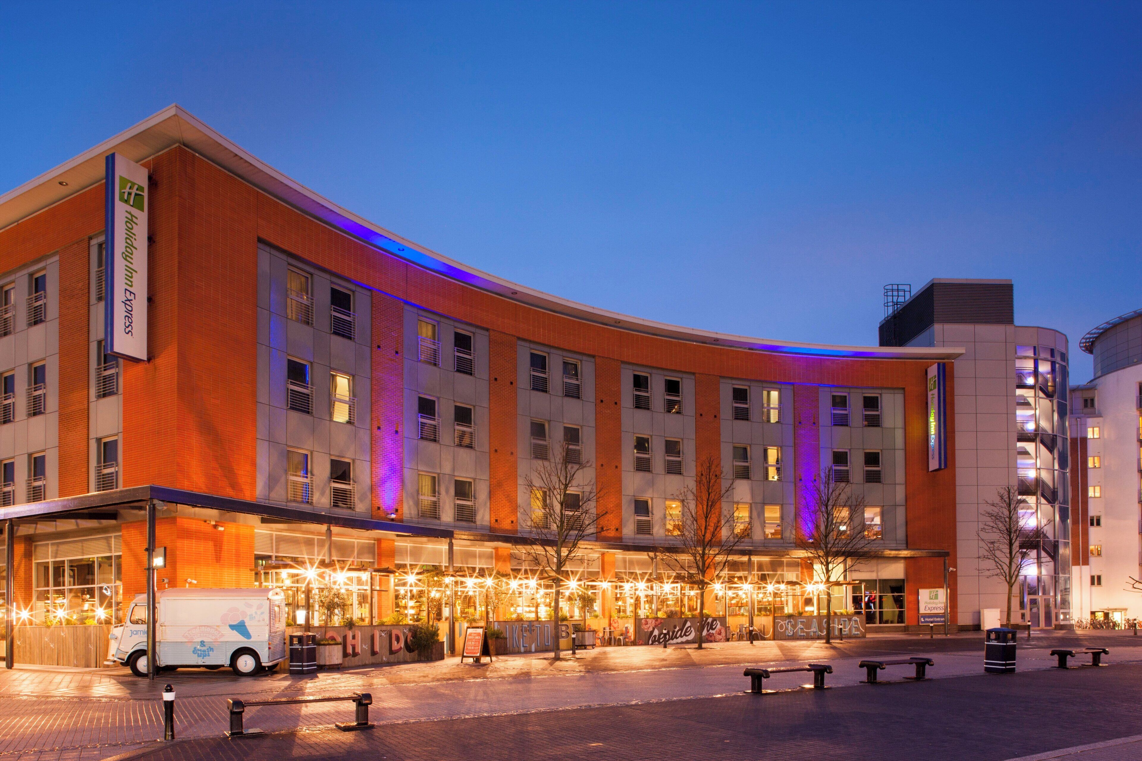 Un hotel de varios pisos con fachada curva, señalización iluminada y un área de entrada cubierta.