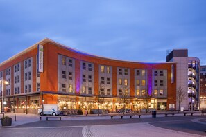 Ein modernes Hotel mit einer geschwungenen Fassade, mehreren Etagen und einem gut beleuchteten Eingangsbereich.