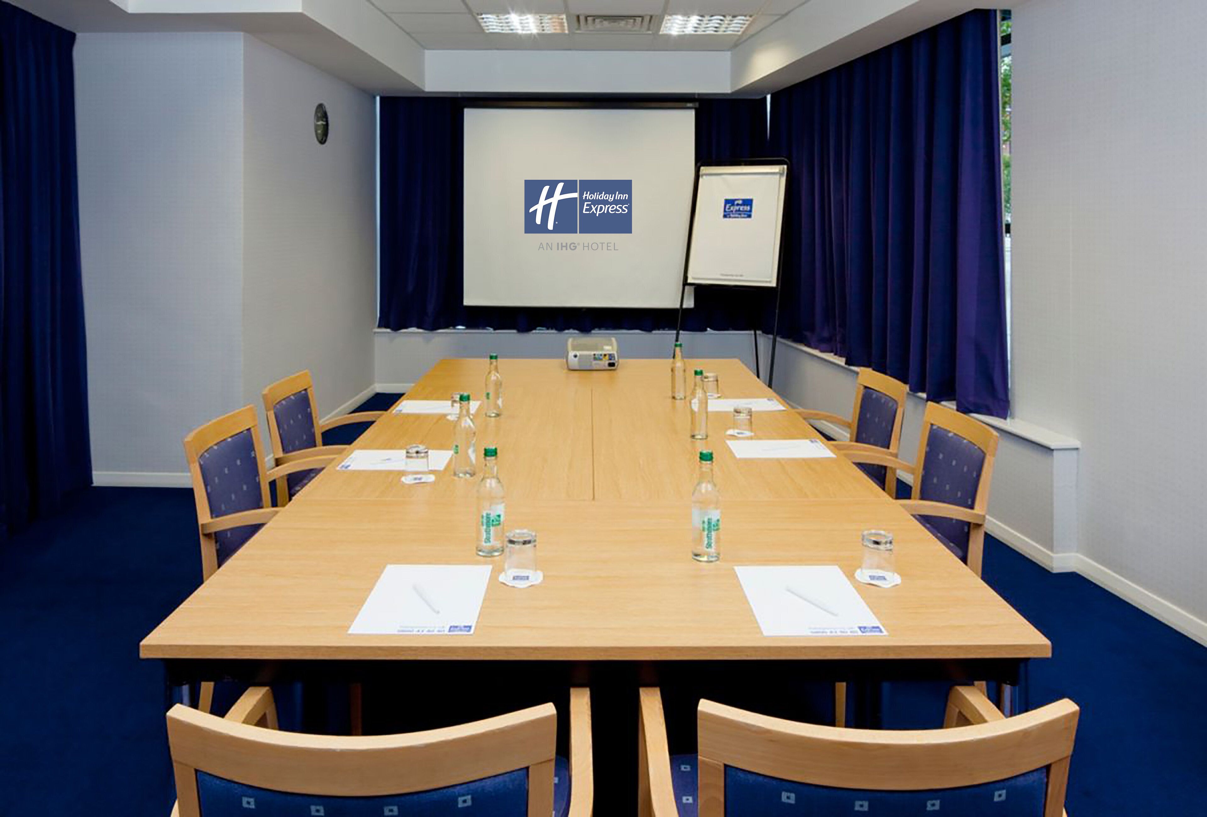 A conference room with a long table, chairs, a projector screen, and a whiteboard.