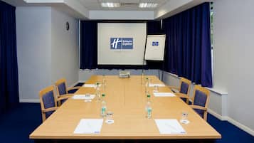 A conference room with a long table, chairs, a projector screen, and a whiteboard.