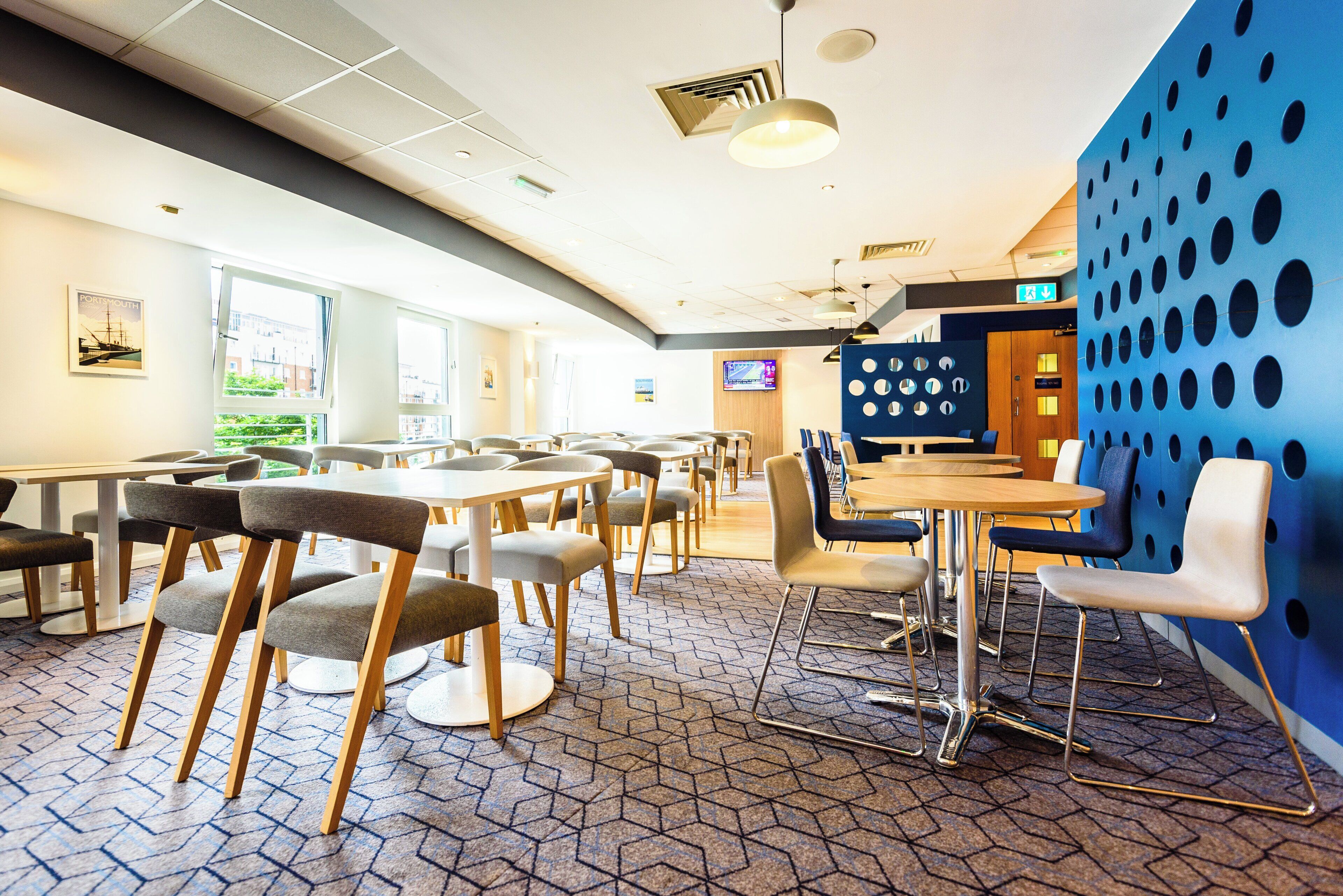 A modern dining area with tables and chairs, a blue accent wall, and a television screen.