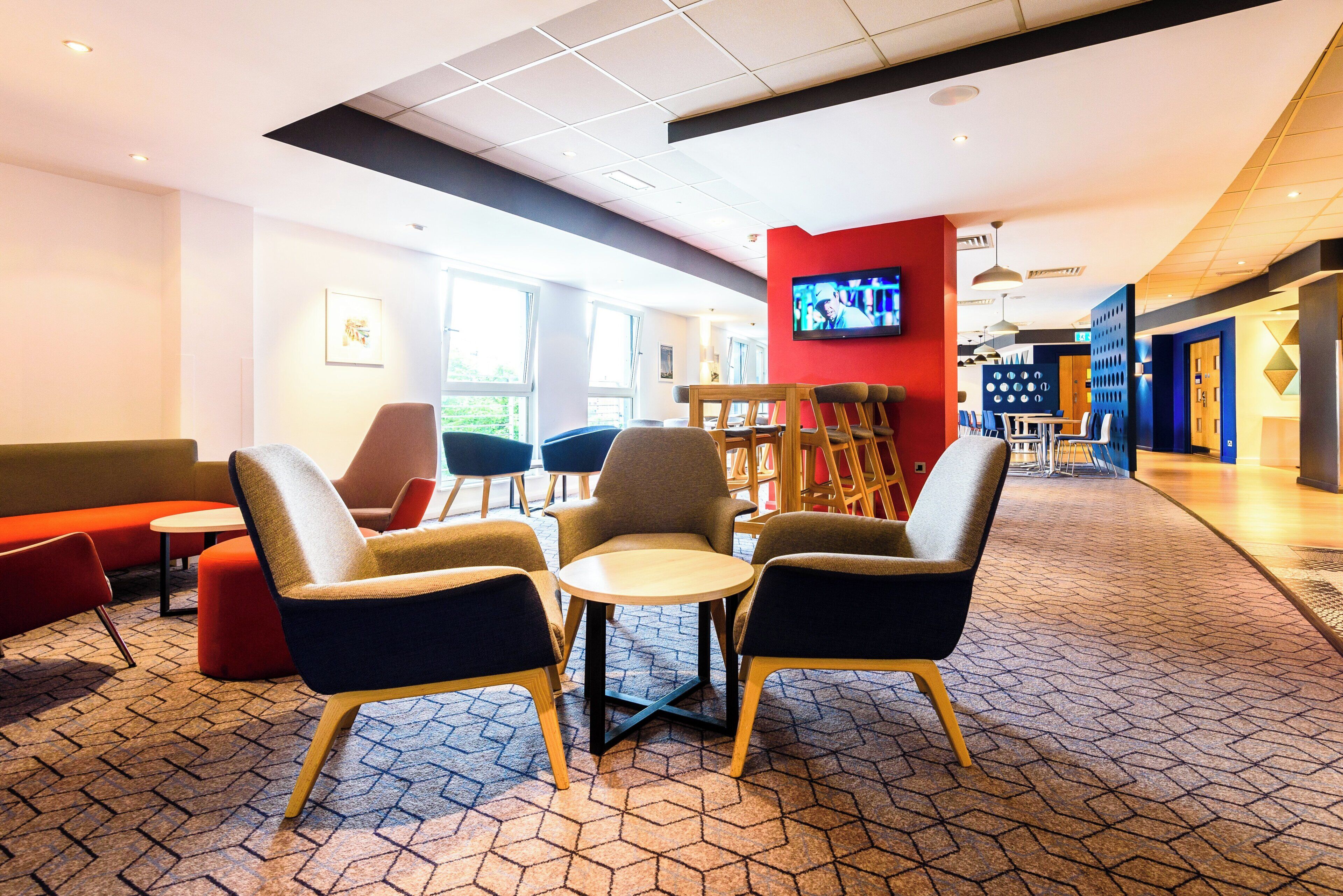 A modern lounge area with seating arrangements, a television screen, and a patterned floor.