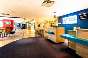 Et Holiday Inn Express receptionsområde med et moderne design, inklusive en receptionsdisk, siddeområde og et tv-skærm.