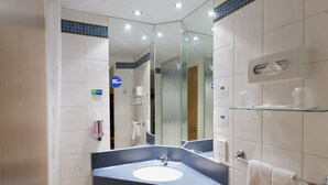 Un baño moderno con un espejo grande, un lavamanos y un estante de vidrio.
