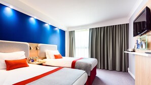 Habitación de hotel con dos camas, televisión, escritorio y ventana con cortinas.