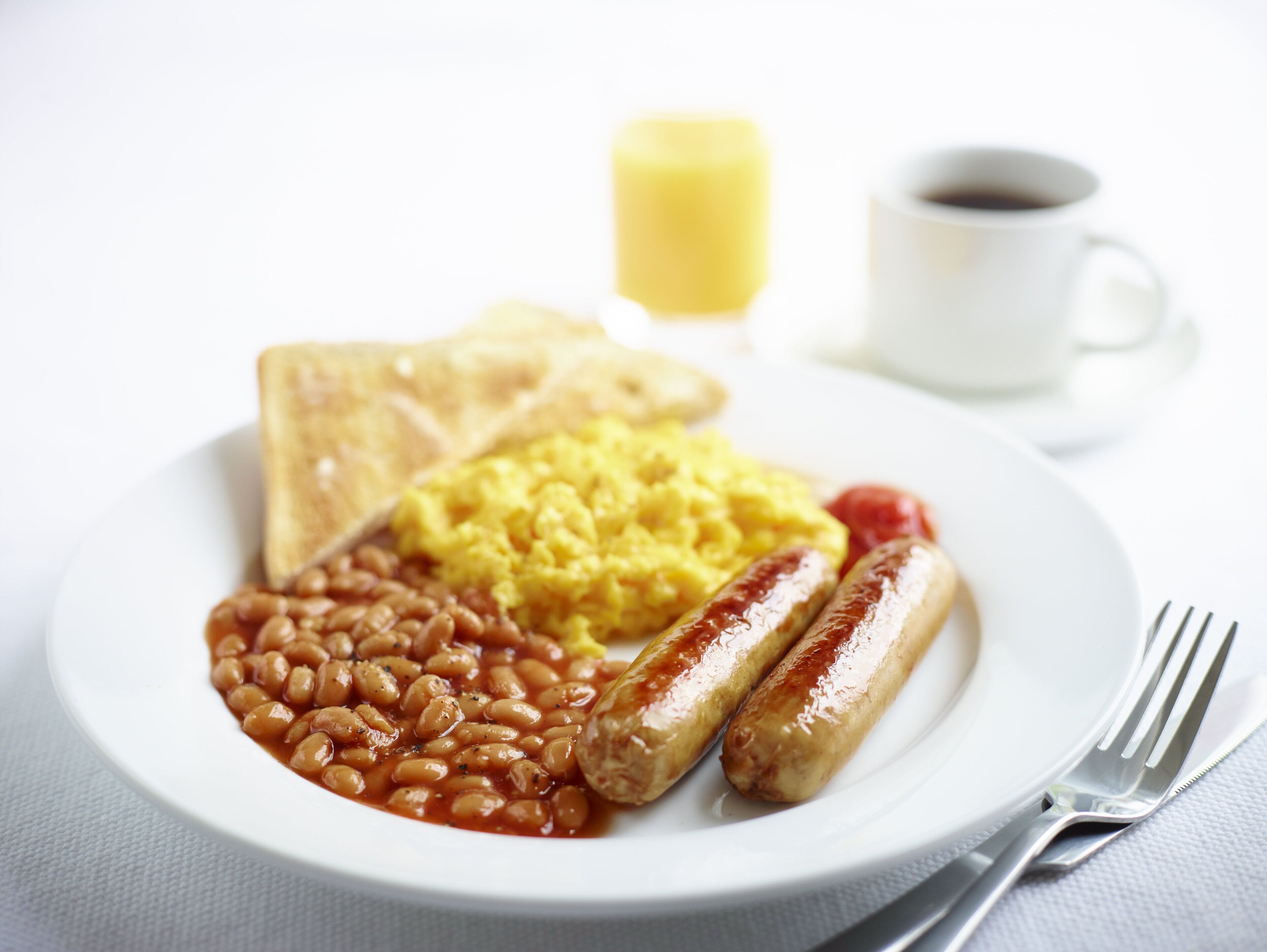 Een bord met toast, roerei, bonen, worstjes en een kop koffie.