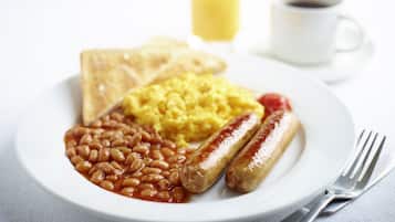 Un piatto con pane tostato, uova strapazzate, fagioli, salsicce e una tazza di caffè.