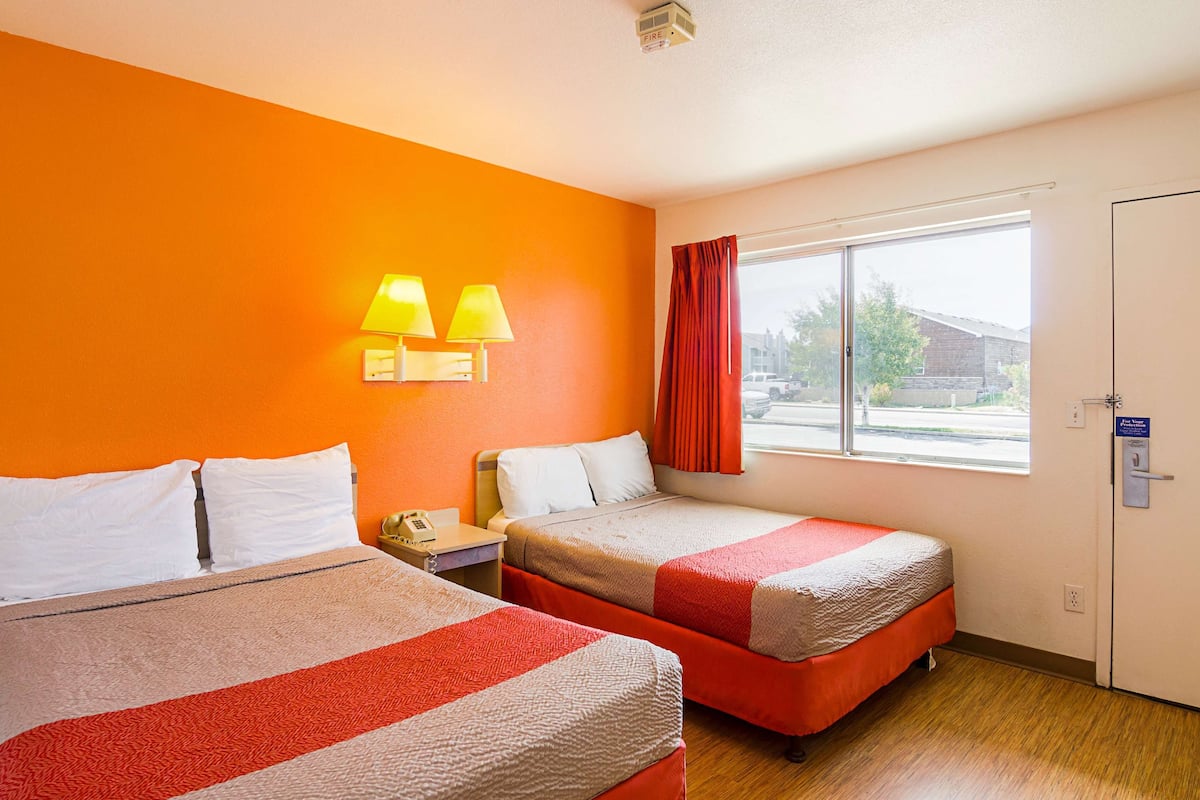 A hotel room with two beds, a window with a view, and a nightstand with a phone.