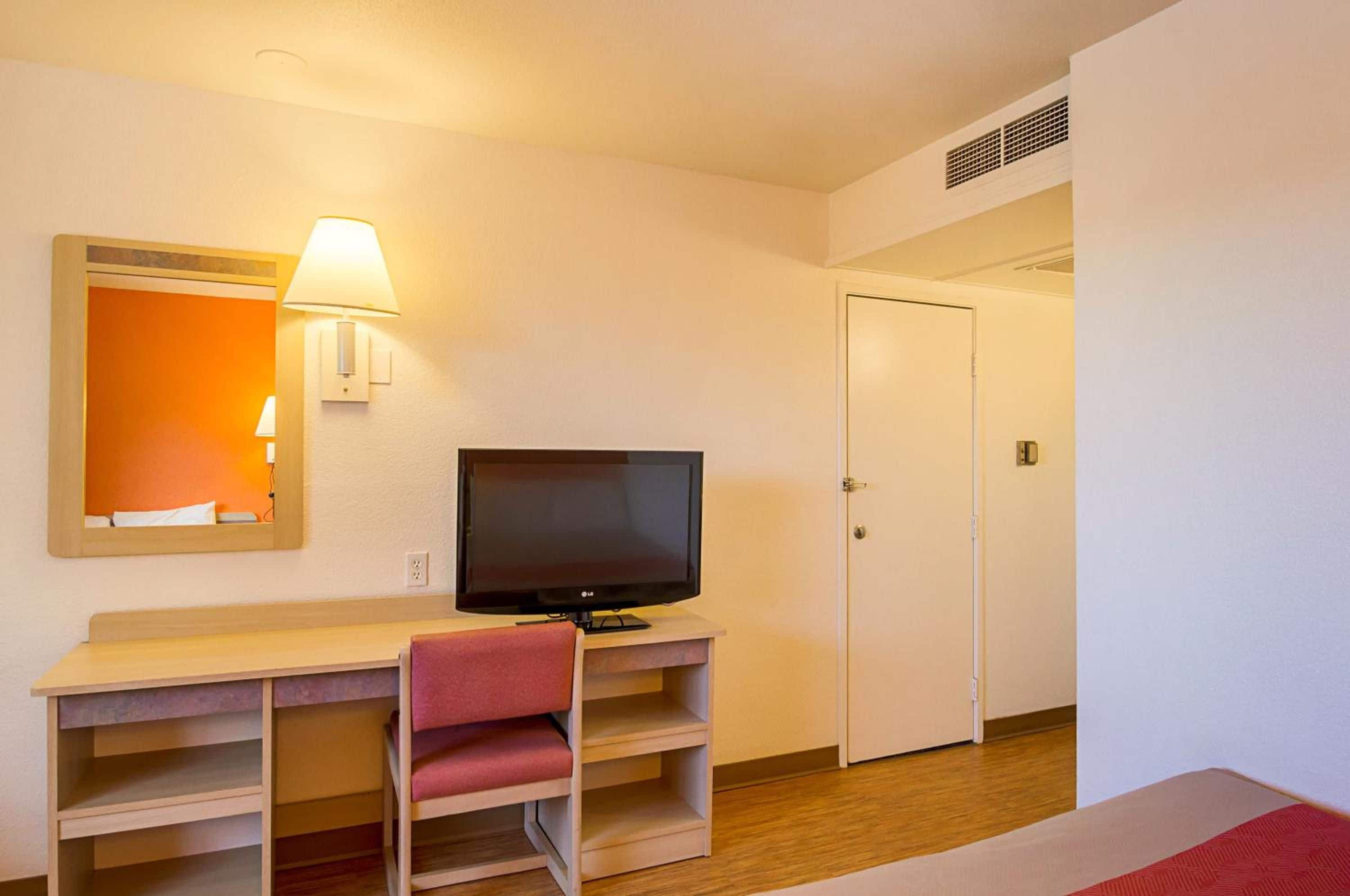 Una habitación de hotel con cama, escritorio con televisor, una silla y una puerta.