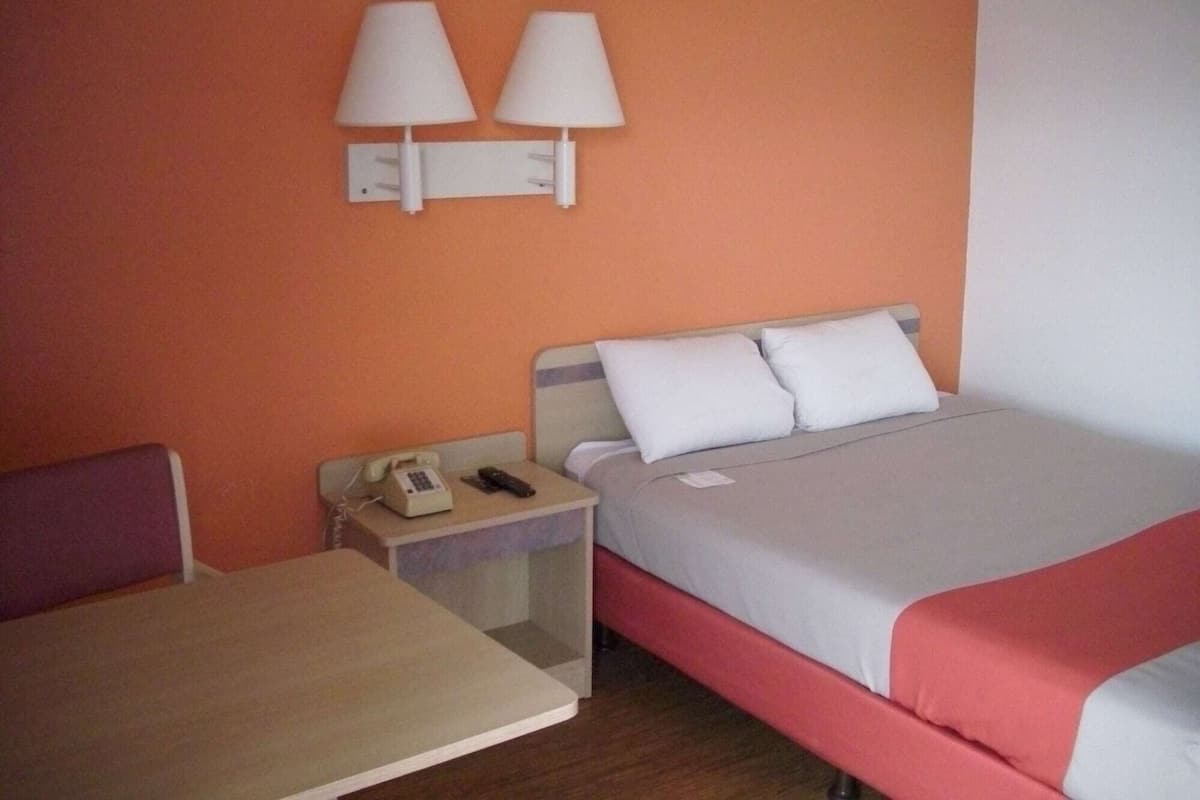 A hotel room with a bed, a bedside table with a phone, and two wall-mounted lamps.