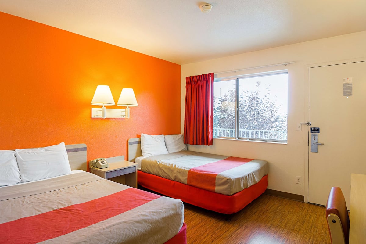 A hotel room with two beds, a window with a view, and a nightstand with a phone.