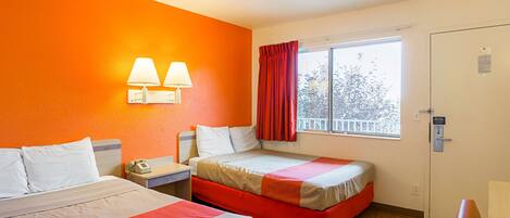 A hotel room with two beds, a window with a view, and a nightstand with a phone.