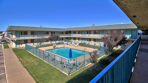 Et motel med swimmingpool, udendørs siddepladser og et hegn.