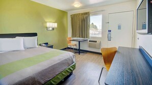 Et hotelværelse med seng, skrivebord, stol, fjernsyn og et vindue med gardiner.