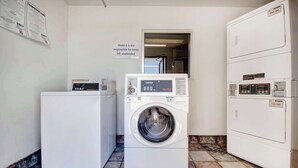 Et vaskerum med en frontbetjent vaskemaskine, en stabelstående tørretumbler, og et skilt der angiver, at motellet ikke er ansvarlig for glemte ejendele.