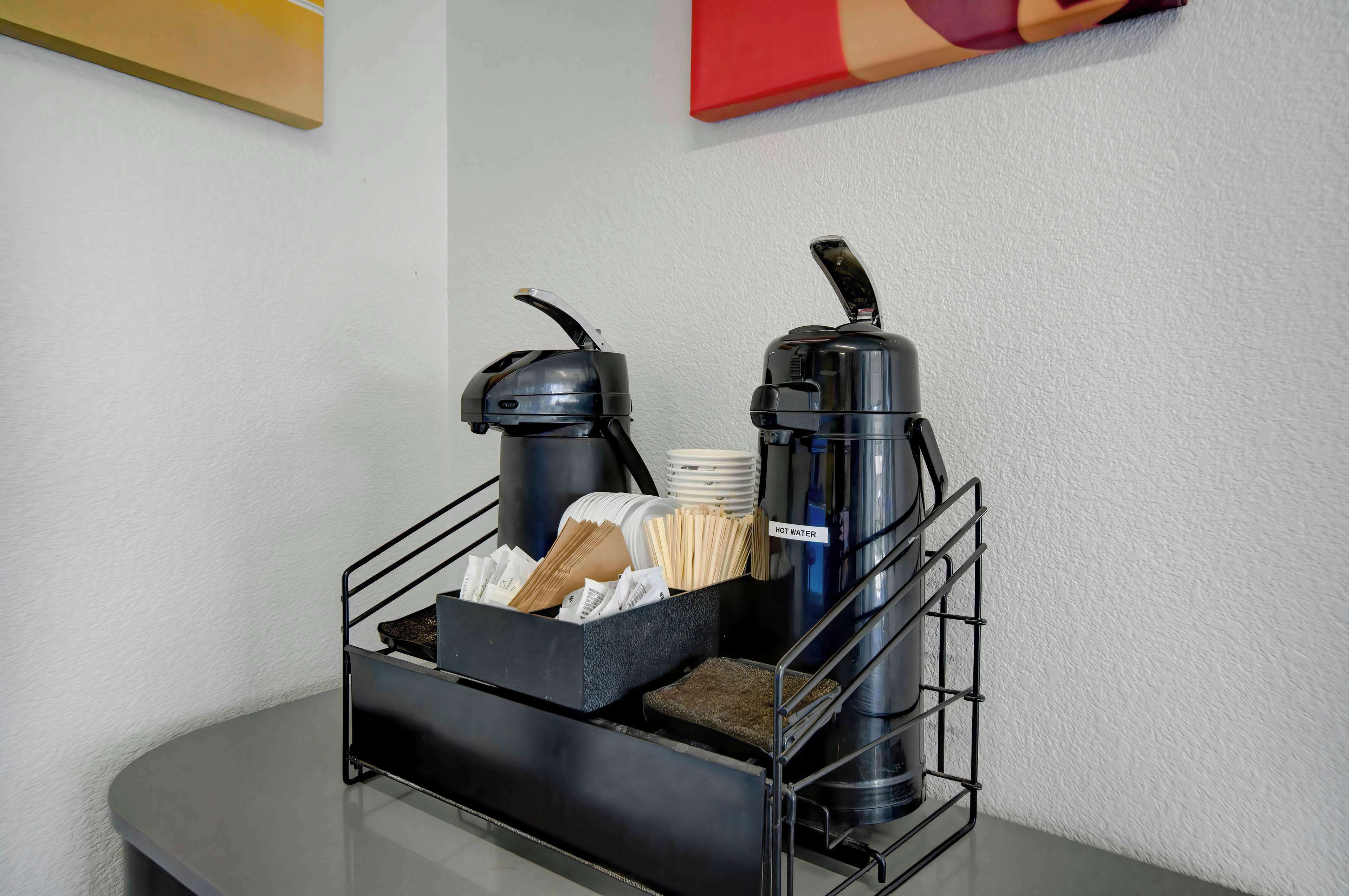 A coffee station with a coffee maker, a water dispenser, and a basket of napkins and tissues.