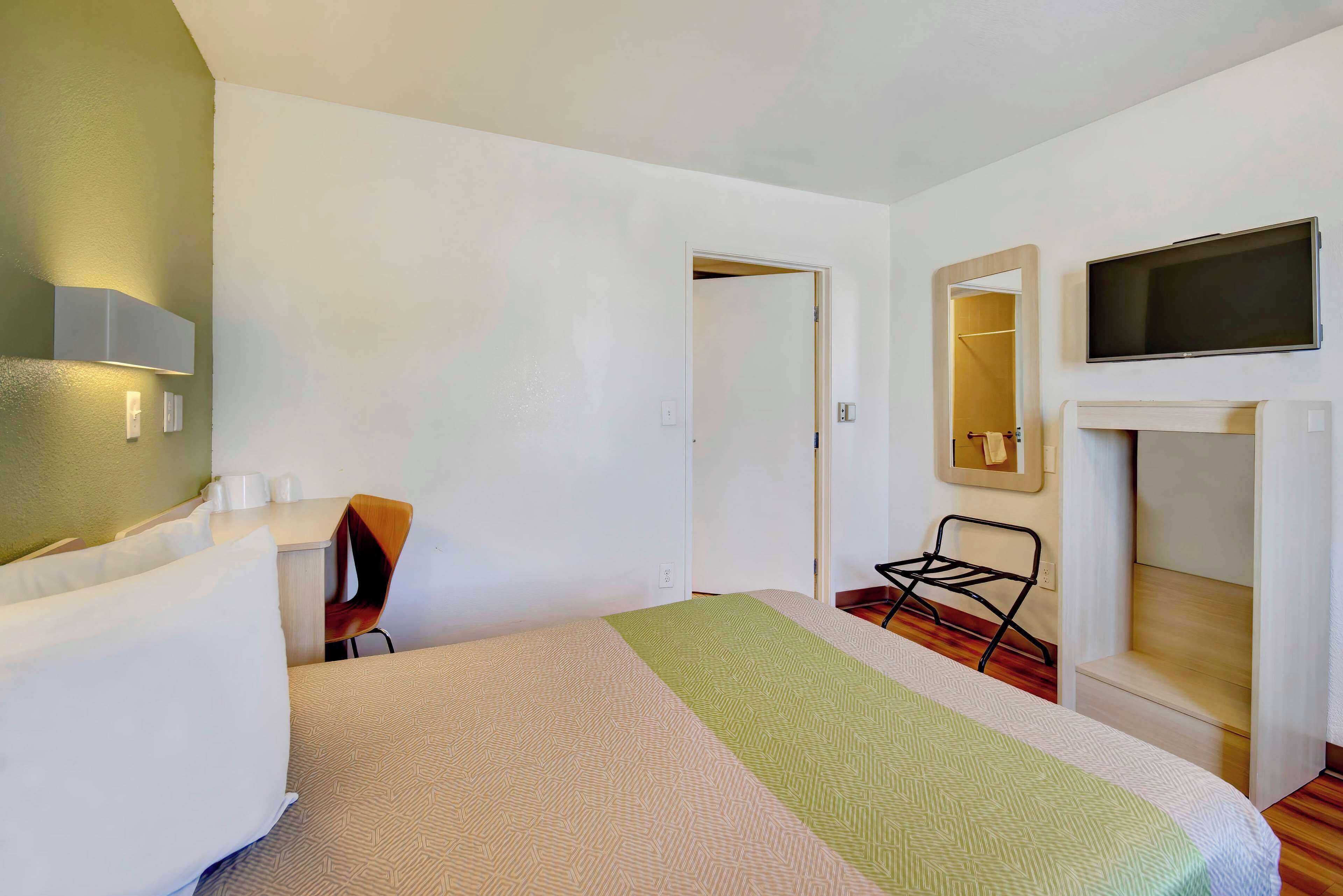 A hotel room with a bed, a chair, a desk, a television, and a mirror.