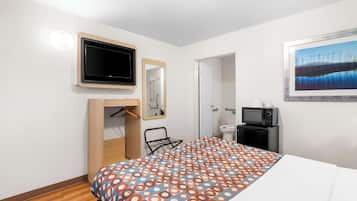 A hotel room with a bed, a television, a mirror, a painting, a wardrobe, and a small desk with a microwave.