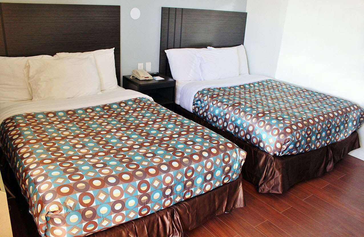 A hotel room with two beds, each with a patterned bedspread and a dark headboard.