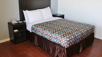 Un lit bien fait, avec une couvre-lit à motifs, une tête de lit sombre et une table de chevet sur laquelle se trouvent un téléphone et un livre.
