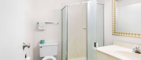 Un baño con inodoro, ducha con mampara de vidrio y lavamanos con espejo.
