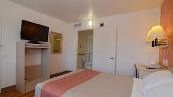 A hotel room with a bed, a TV mounted on a cabinet, a bedside table with a lamp, and a bathroom visible through an open door.