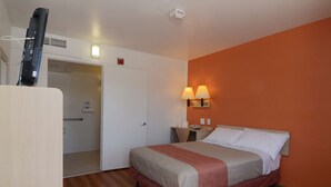 Une chambre d’hôtel comprenant un lit, un téléviseur posé sur un meuble, une porte donnant accès à une salle de bain et deux lampes fixées au mur.