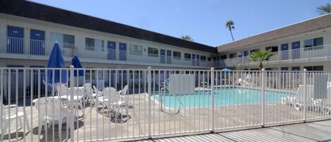 Un motel con piscina, cercas blancas y sillas al aire libre.