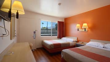 A hotel room with two beds, a desk, a chair, a window with a view of the street, and two wall-mounted lamps.