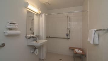 A bathroom with a sink, mirror, shower, and a bench with towels.