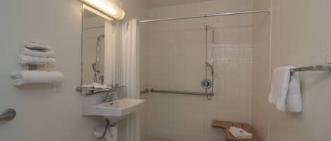 A bathroom with a sink, mirror, shower, and a bench with towels.