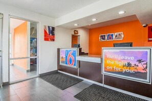 Ein Hotel-Empfangsbereich mit Glastür, Empfangstresen und einer Wand mit gerahmten Bildern und einem motivierenden Zitat.