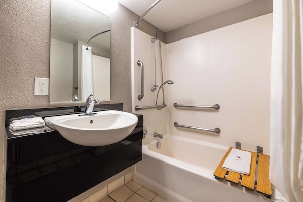 A bathroom with a white sink, mirror, and bathtub. There are grab bars on the tub and a towel rack.