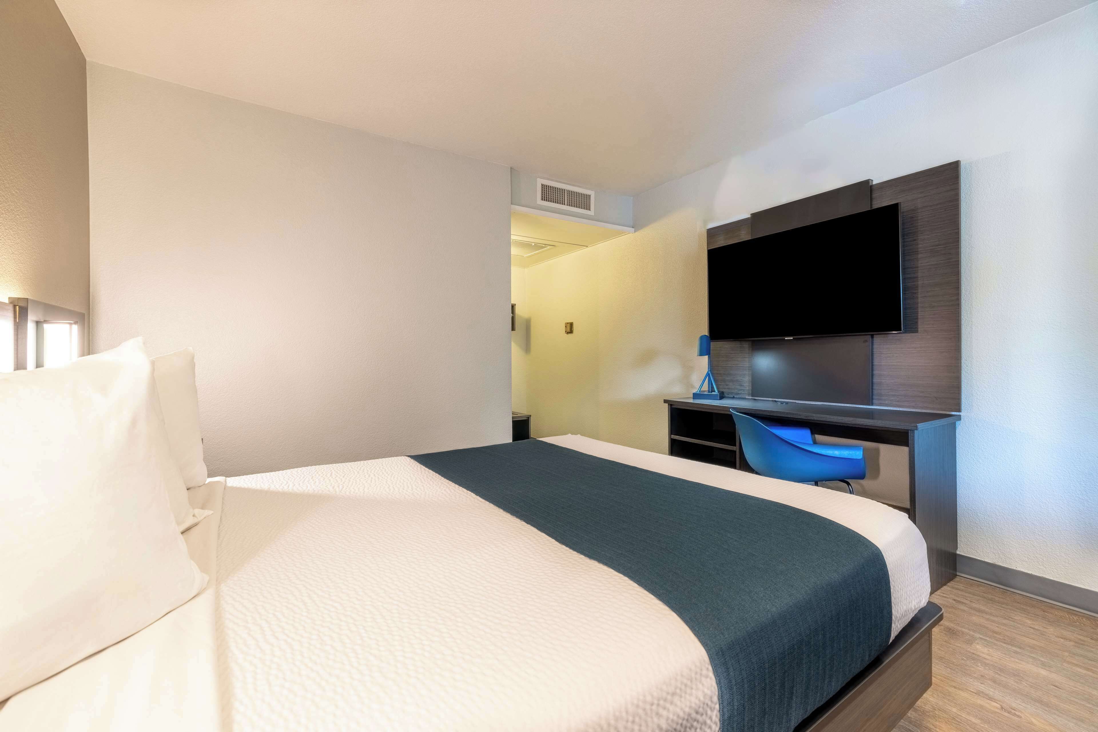 Ein Hotelzimmer mit einem Bett, einem Schreibtisch und einem an der Wand befestigten Flachbildfernseher.