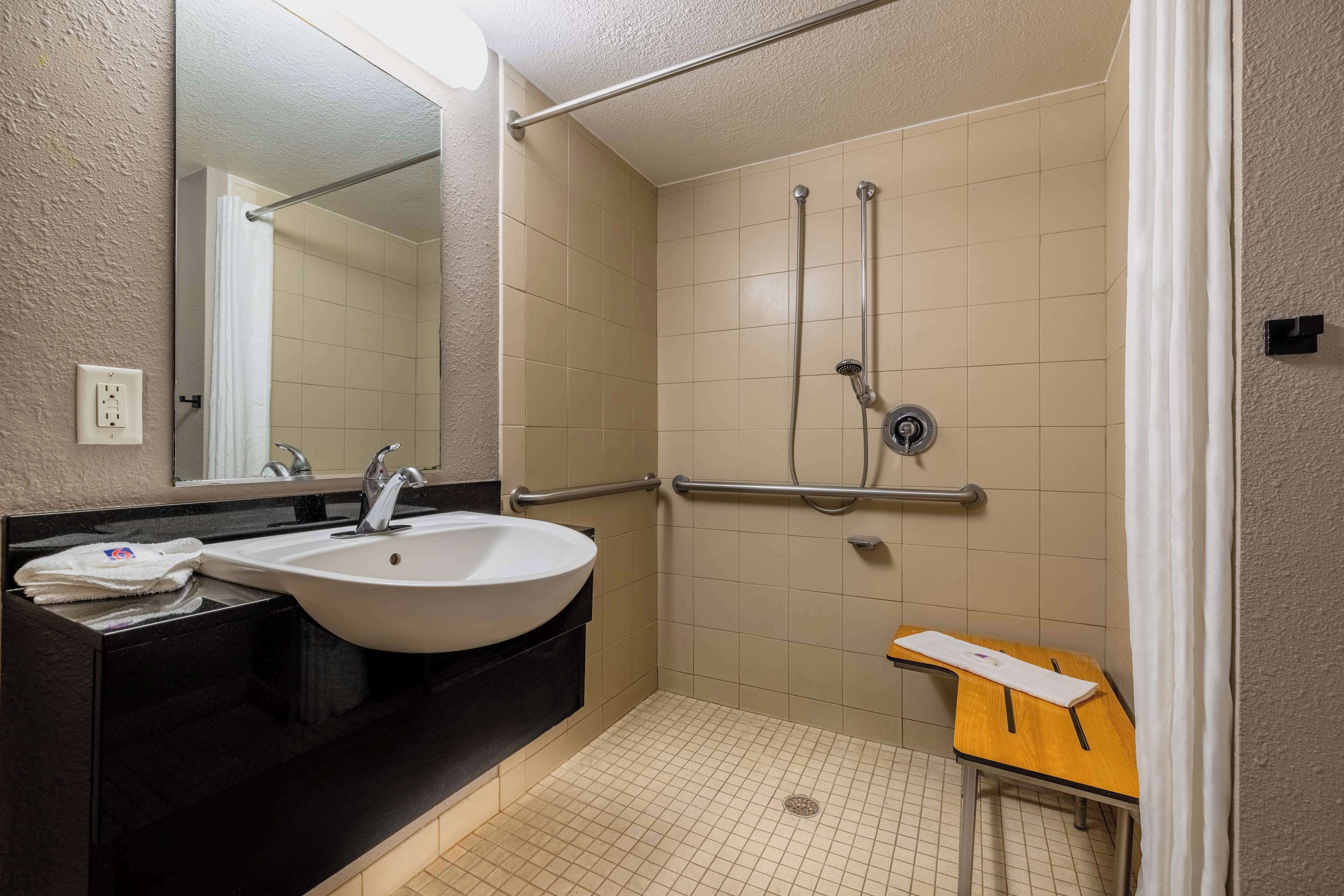 A bathroom with a sink, mirror, shower, and a small table.