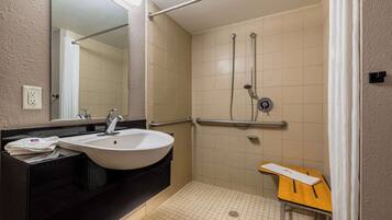 Une salle de bain avec un lavabo, un miroir, une douche et une petite table.