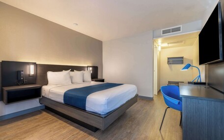 Una habitación de hotel moderna con cama, mesita de noche, lámpara y un escritorio con silla.