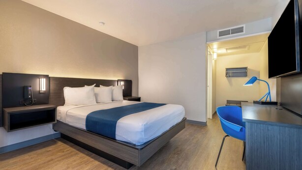 Una habitación de hotel moderna con cama, mesita de noche, lámpara y un escritorio con silla.