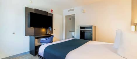 A hotel room with a bed, a desk, a television, and a minibar.