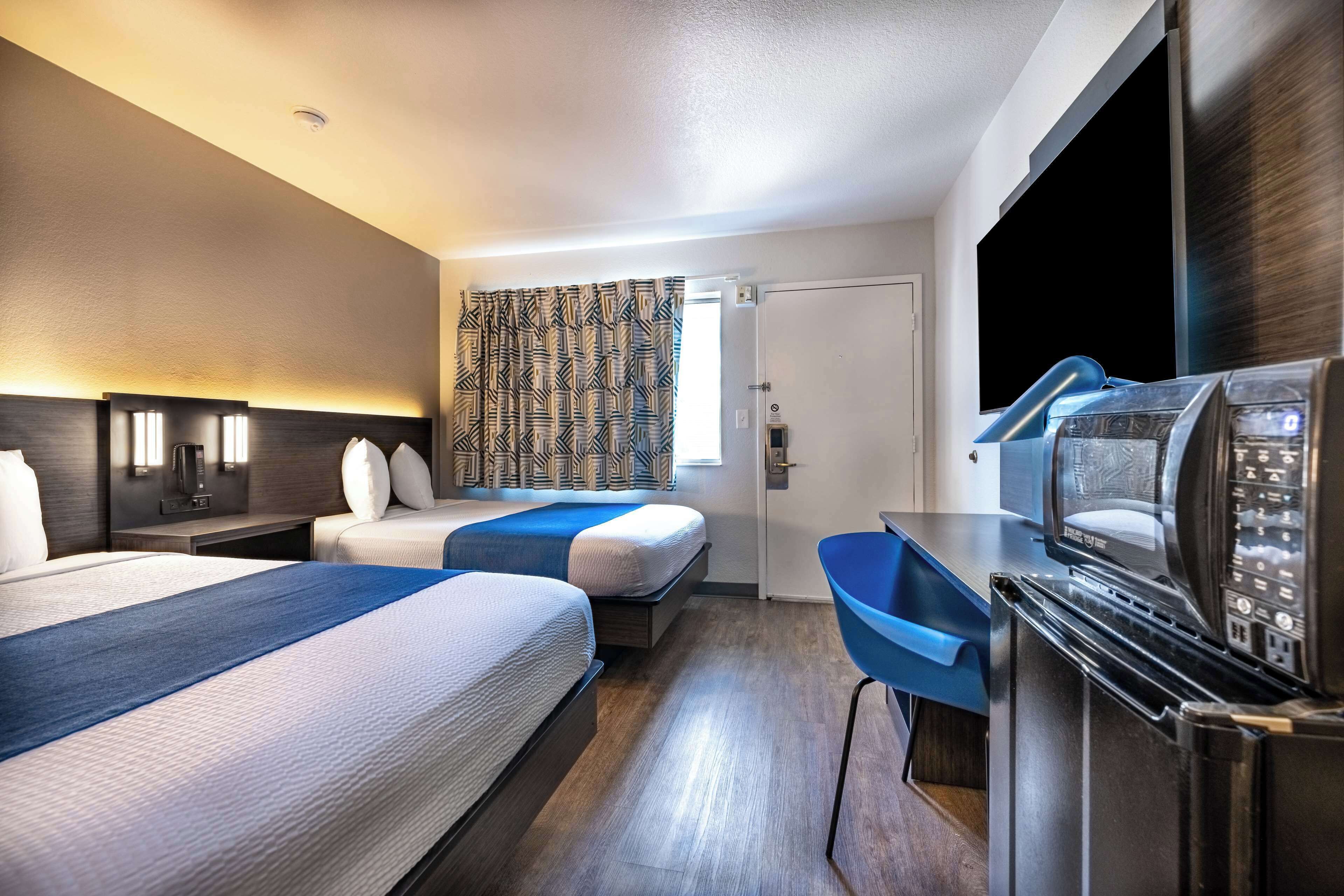 Habitación de hotel con dos camas, un escritorio, un microondas y un televisor.