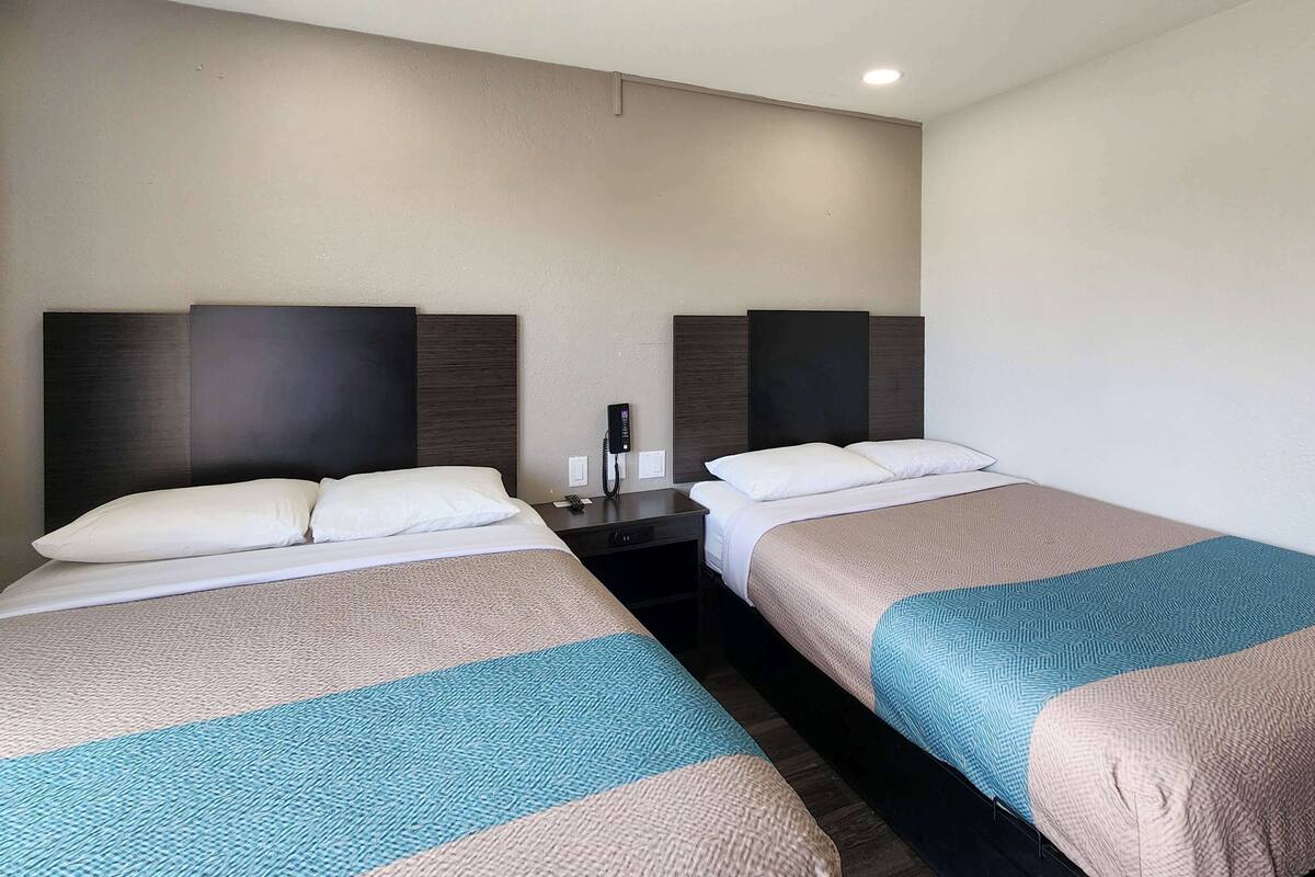 A hotel room with two single beds, each with a headboard, bedside tables, and a telephone.