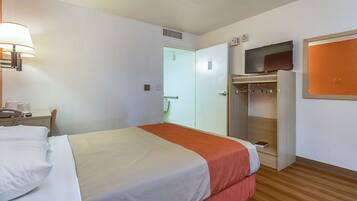 Una habitación de hotel con cama, mesita de noche con lámpara, televisor montado en la pared y armario.
