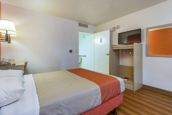 A hotel room with a bed, a bedside table with a lamp, a TV mounted on the wall, and a wardrobe. - Motel 6 Phoenix North - Bell Road (Phoenix)